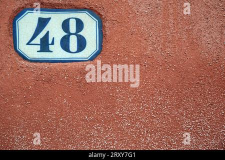 The number 48 on a white ceramic panel set into the render of a red painted wall shot close up full frame but leaving copy space. Stock Photo
