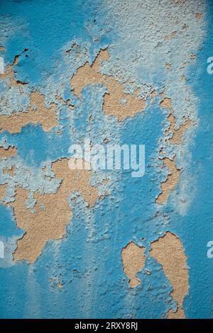 The blue paint peeling away from a sandy plaster surface of a wall, shot in portrait format for use as a background Stock Photo