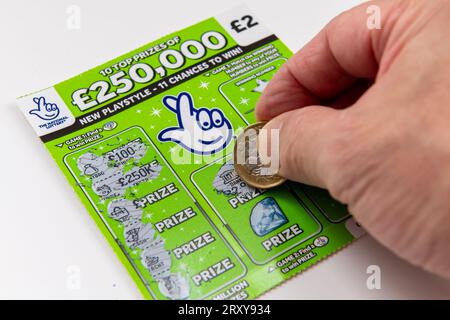 London. UK- 09.27.2023. A National Lottery scratch cards isolated in white with a player using a coin to scratch the card. Stock Photo