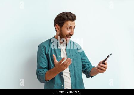 Surprised man showing happy gesture while looking to his mobile phone on white background Stock Photo