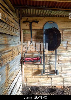 A manual lawn mower and a  basic black grill hanging from a cane wall in a rustic shed, in a farm near the colonial town of Villa de Leyva. Stock Photo