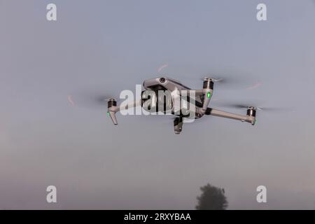 A small foldable drone in flight mode with the spot lights on.. A gray drone in flight in the air. Gray drone in flight in the air. quadrocopter with Stock Photo