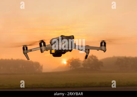 A small foldable drone in flight mode with the spot lights on.. A gray drone in flight in the air. Gray drone in flight in the air. quadrocopter with Stock Photo