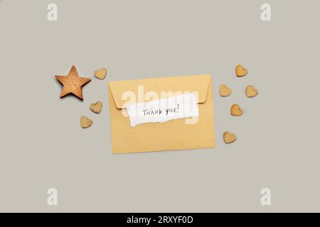 A brown envelope with a thank you note and a wooden star and hearts on a gray background Stock Photo