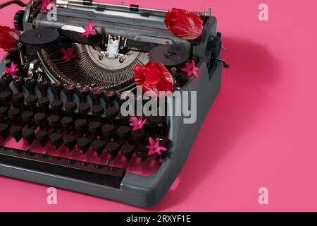 Vintage typewriter with pink flowers and red tulips on color background Stock Photo
