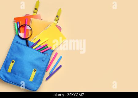 School backpack with different stationery on pale yellow background Stock Photo