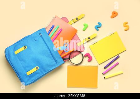School backpack with different stationery on pale yellow background Stock Photo