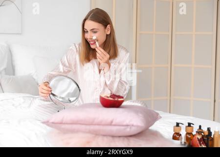 Young woman massaging face in bedroom Stock Photo