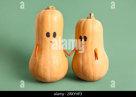 Cute pumpkins with drawn faces holding hands on green background Stock Photo