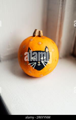 cute little orange pumpkin with painted black cat face, gold polka dots Stock Photo