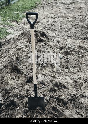 Shovel is stuck into pile of earth. Fresh grave or burial in cemetery. Background. Stock Photo