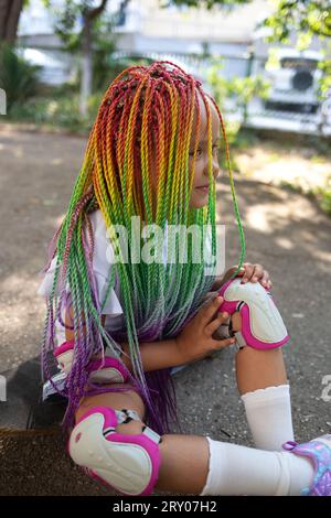 little cute girl with colorful afro pigtails sits on a skateboard Stock Photo