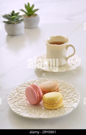 Delicate pastel coloured macaroons with dainty cup of tea on marble background in vertical format. Stock Photo
