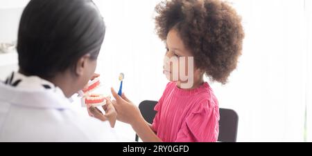 African American dentist explaining to mixed-race afro child how to brush teeth. The doctor and healthcare concept for children. Stock Photo