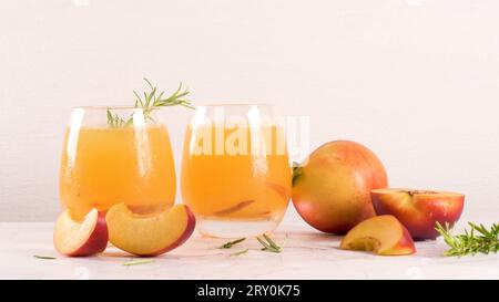 Homemade peach juice with ice cubes and rosemary leaves in glass on marble stone background. Stock Photo