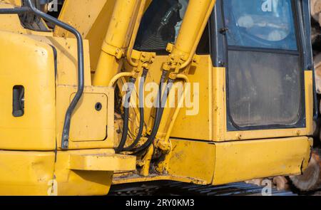 Closeup detail of a working, used, dirty yellow excavator, centered on hydraulics hoses and pipes next to the window of the operator cab. Stock Photo