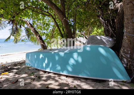 Blue boat lay upside down in the shadow on the beach Stock Photo