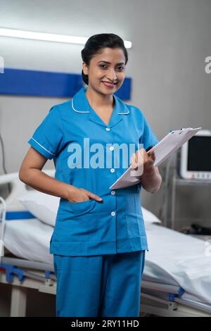 vertical shot Happy Smiling Nurse with Clipboard standing confidently by looking camera at hospital - Concept of professional occupation, Medical Stock Photo