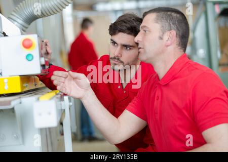 man explaining controls of industrial machine to younger worker Stock Photo