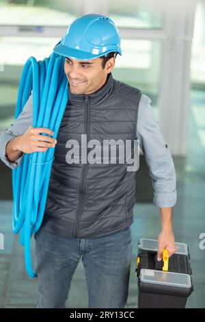 builder carrying reel of blue pipe on his shoulder Stock Photo