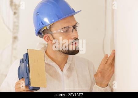 builder in hardhat sanding wall indoors Stock Photo