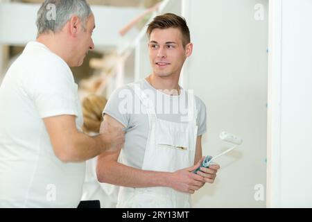 painter teaching roller technique to apprentice decorator Stock Photo