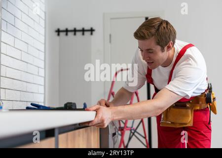 Gloved craftsman installs hob in kitchen. Household Appliance Installation Services Concept Stock Photo