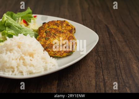 Oatmeal fritters with vegetables and white rice served on a plate on a wooden table. Healthy food. Stock Photo