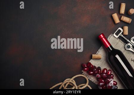 Bottle of wine, red grapes, corkscrew and corks, on rusty background top view, copy space Stock Photo