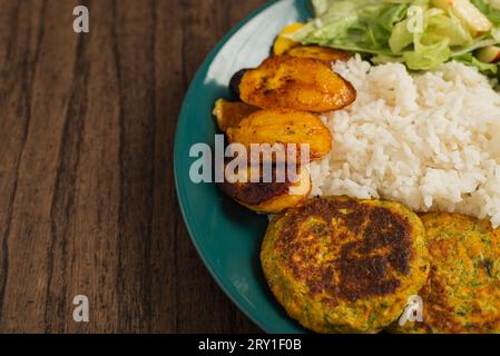 Oatmeal fritters with vegetables, fried ripe bananas and white rice served on a plate on a wooden table. Healthy food. Stock Photo