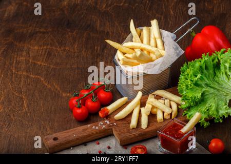 French fries in a grid with ketchup, salad and cherry tomatoes on wooden brown table. Top view. Stock Photo