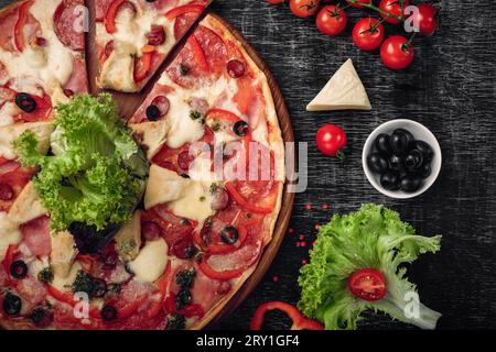 Pizza with ham, salami, cheese, mushrooms, cherry tomatoes, bell peppers and salad on a black chalk board, top view. Stock Photo