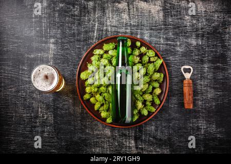 A bottle of beer on a green fresh hop in a plate against the background of a black scratched chalkboard, top view. Stock Photo