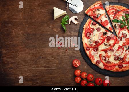 Pizza with smoked sausages, cheese, mushrooms, cherry tomatoes, bell peppers and greens on a stone and a wooden brown board, top view. Stock Photo