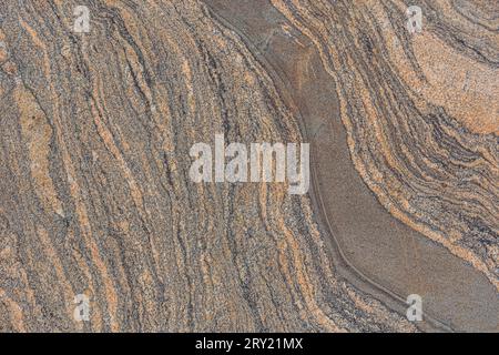 Wavy pattern from a brown granite stone. Background pattern natural stone with broken lines. Surface with dark color interruptions. Diagonally meander Stock Photo