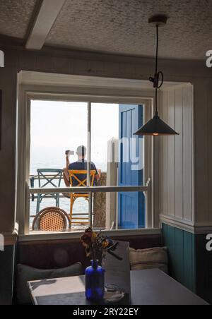 A visitor outside the Devonport Inn at Kingsand keeps in touch whilst relaxing beside Cawsand Bay Stock Photo