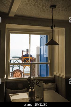 A cool guy outside the Devonport Inn at Kingsand keeps in touch whilst relaxing beside Cawsand Bay. Sepia and color mix Stock Photo