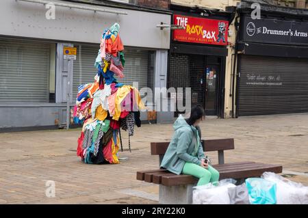 Artist Jeremy Hutchison performs as a 'monster sculpture' as part of his work Dead White Man which explores the global trade in second-hand clothes, as he walks through Blackburn town centre to promote the British Textile Biennial 2023 at the Cotton Exchange, Blackburn, a building once used to sell raw cotton from American plantations to the mill owners of Lancashire. Picture date: Thursday September 28, 2023. Stock Photo