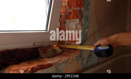 taking measurements from the window opening after installing the window using a tape measure, measuring the width and depth of the opening Stock Photo
