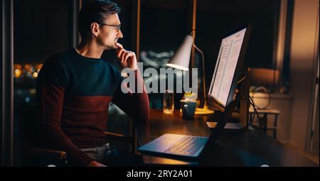A caucasian businessman works late at his home office, focused on a marketing project. Sitting at his desk with a laptop, he plans and strategizes wit Stock Photo