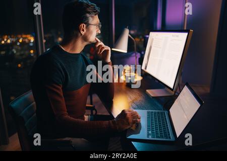 A caucasian business man works late at the office, strategizing and planning a marketing project on his laptop. The atmosphere is quiet and thoughtful Stock Photo