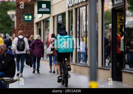 delivery cyclist in Exeter city high street shopping centre whilst busy during the day time - Deliveroo Stock Photo