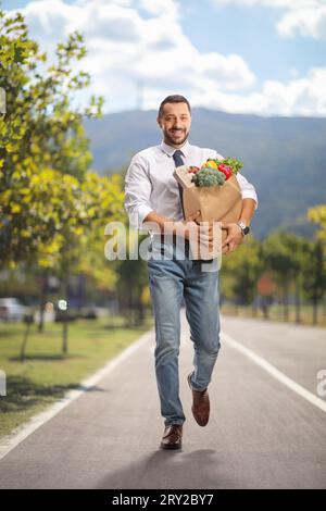 Full length portrait of a young professional man carrying a grocery bag and walking at a pedestrian lane Stock Photo