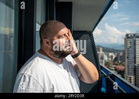 Fat man suffers dying from heat. Guy on balcony under hot summer sun sweats from high temperatures Stock Photo