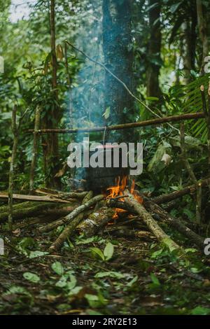 Campsite fireplace with pot hanging on stick above burning logs in tropical rainforest Stock Photo