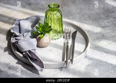 High angle of minimalist table setting with small potted plant on plate with cutlery and empty bottle in sunlight Stock Photo