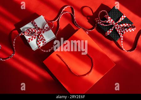 From above small colored cardboard boxes with red bow placed on red background next to a gift bag Stock Photo