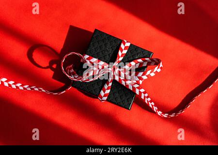 From above small black colored cardboard box with red bow placed on red background Stock Photo