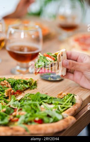 Selective focus of crop person eating appetizing pizza with cheese and lettuce on wooden table with glasses of wine Stock Photo