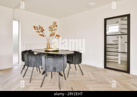 Interior of stylish modern dining room with flower vases on round table and black chairs located next to door in light apartment Stock Photo